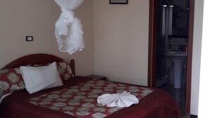 A bedroom with a bed, a canopy, a framed picture on the wall, and a bathroom door.