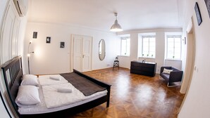 A spacious bedroom with a large bed, a dresser, a chair, and a desk. There are multiple windows providing natural light. - St. Nicholas Church view apartment (Prague)