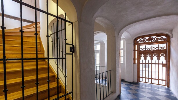 A staircase with metal railings leading to a room with a checkered floor and a decorative wooden gate. - St. Nicholas Church view apartment (Prague)