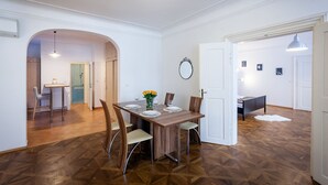 A dining area with a wooden table, chairs, and a vase of flowers. There is a mirror on the wall and a door leading to another room. - St. Nicholas Church view apartment (Prague)