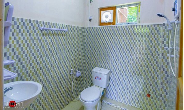 A bathroom with a checkered tile wall, a toilet, a sink, and a shower. - Hein Motel (Meiktila)