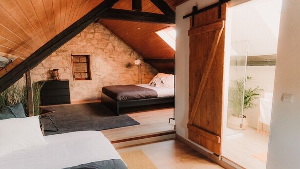 Un dormitorio acogedor en el ático con pared de piedra, cama, escritorio y una ventana grande.