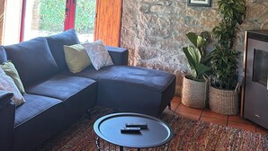 Una sala de estar con pared de piedra, techo de madera, un sofá modular, una mesa redonda de centro y una televisión.