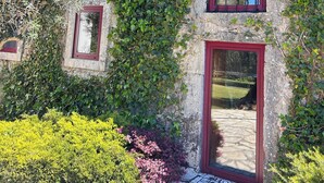 Un edificio de piedra con techo de tejas rojas, puerta enmarcada en rojo y una ventana con marco rojo.