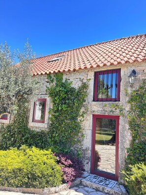 A stone building with a red-tiled roof, a red-framed door, and a window with a red frame.