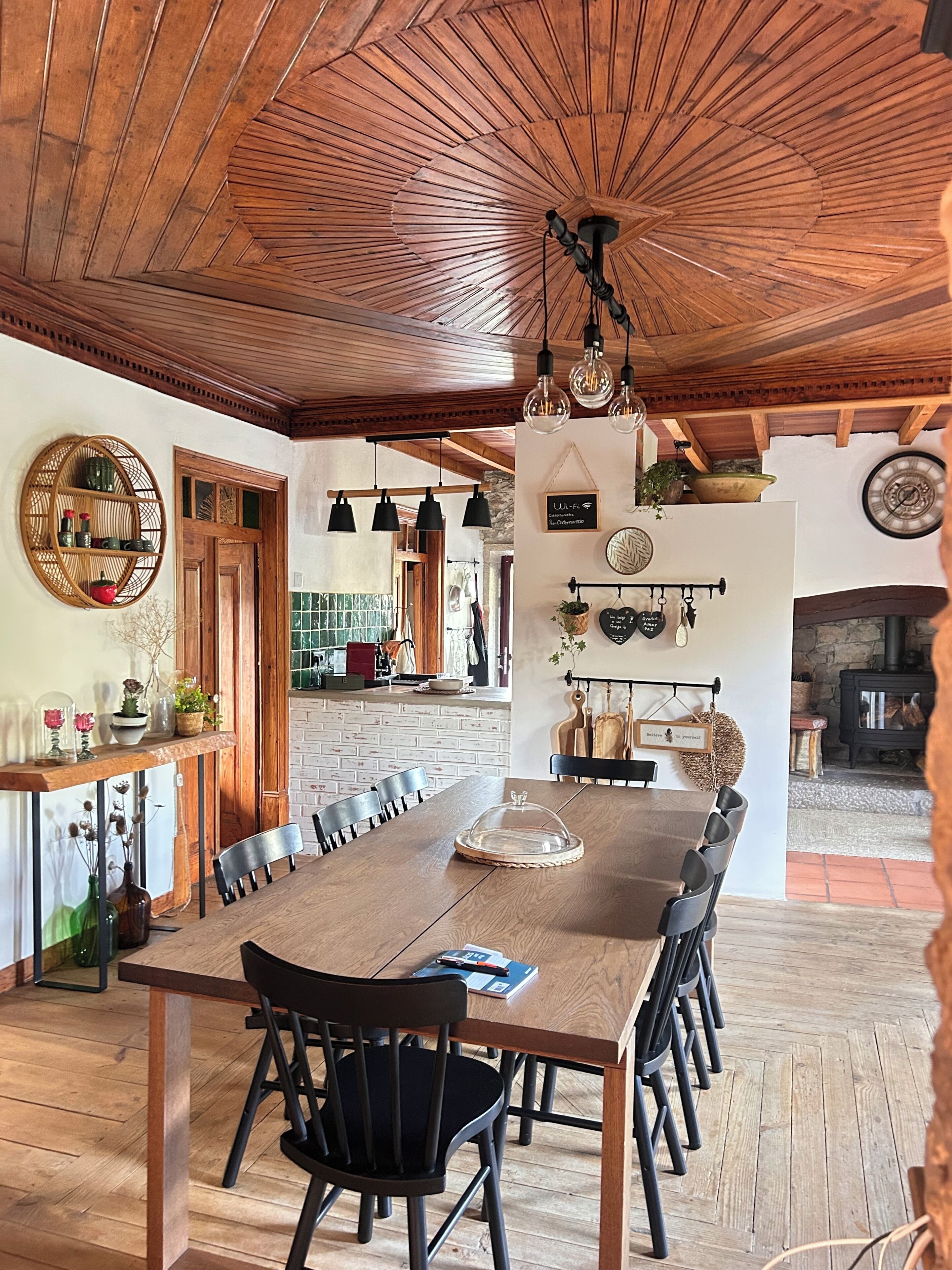 A spacious dining area with a long wooden table, black chairs, and hanging pendant lights.