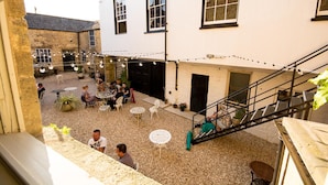 A courtyard with outdoor seating, a staircase, and a building with large windows. - The Crooked Swan (Crewkerne)