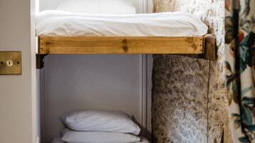 Een stapelbed met witte beddengoed in een kamer met stenen muren en een bloemen gordijn.