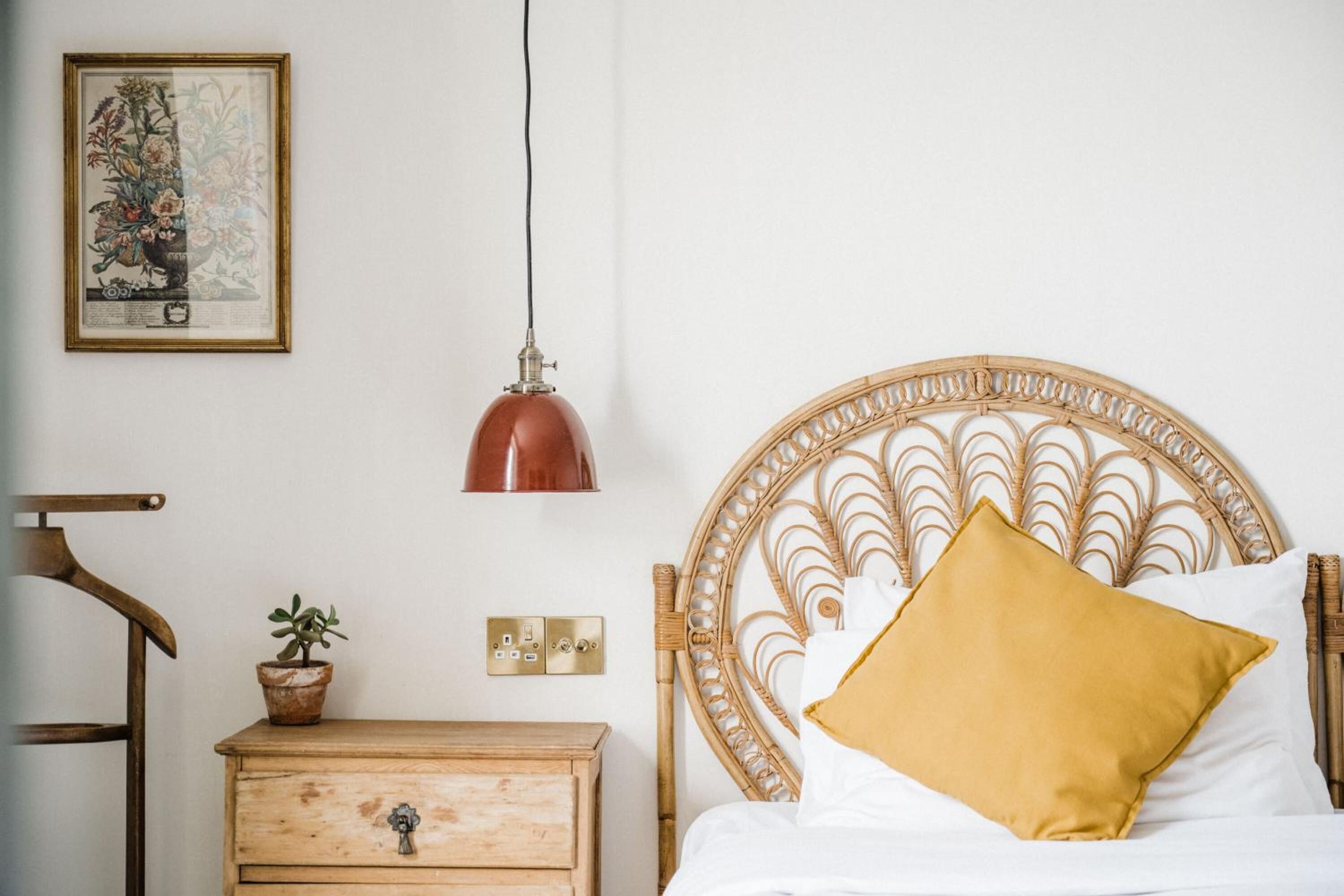 A bedroom with a wooden headboard, a bedside table with a plant, a lamp, and a framed picture on the wall.
