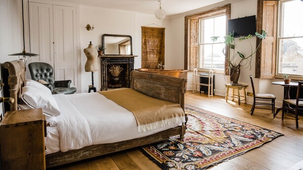 A bedroom with a wooden bed, a large mirror, a dresser, and a television on the wall. - The Crooked Swan (Crewkerne)