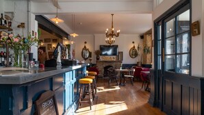 A bar area with stools, a television, and a fireplace. - The Crooked Swan (Crewkerne)