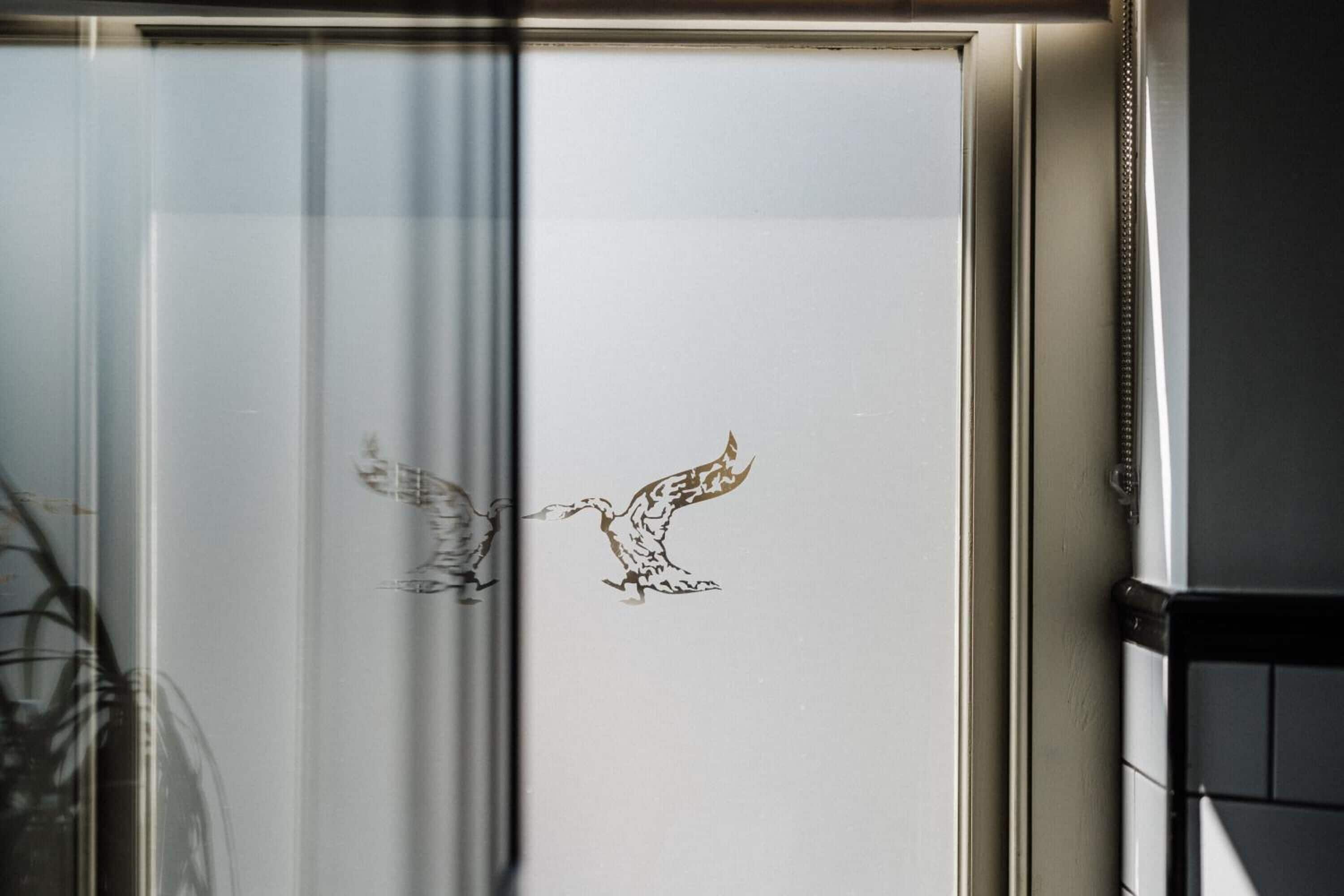 Een raam met een kunstwerk waarop twee vogels in de vlucht staan afgebeeld.