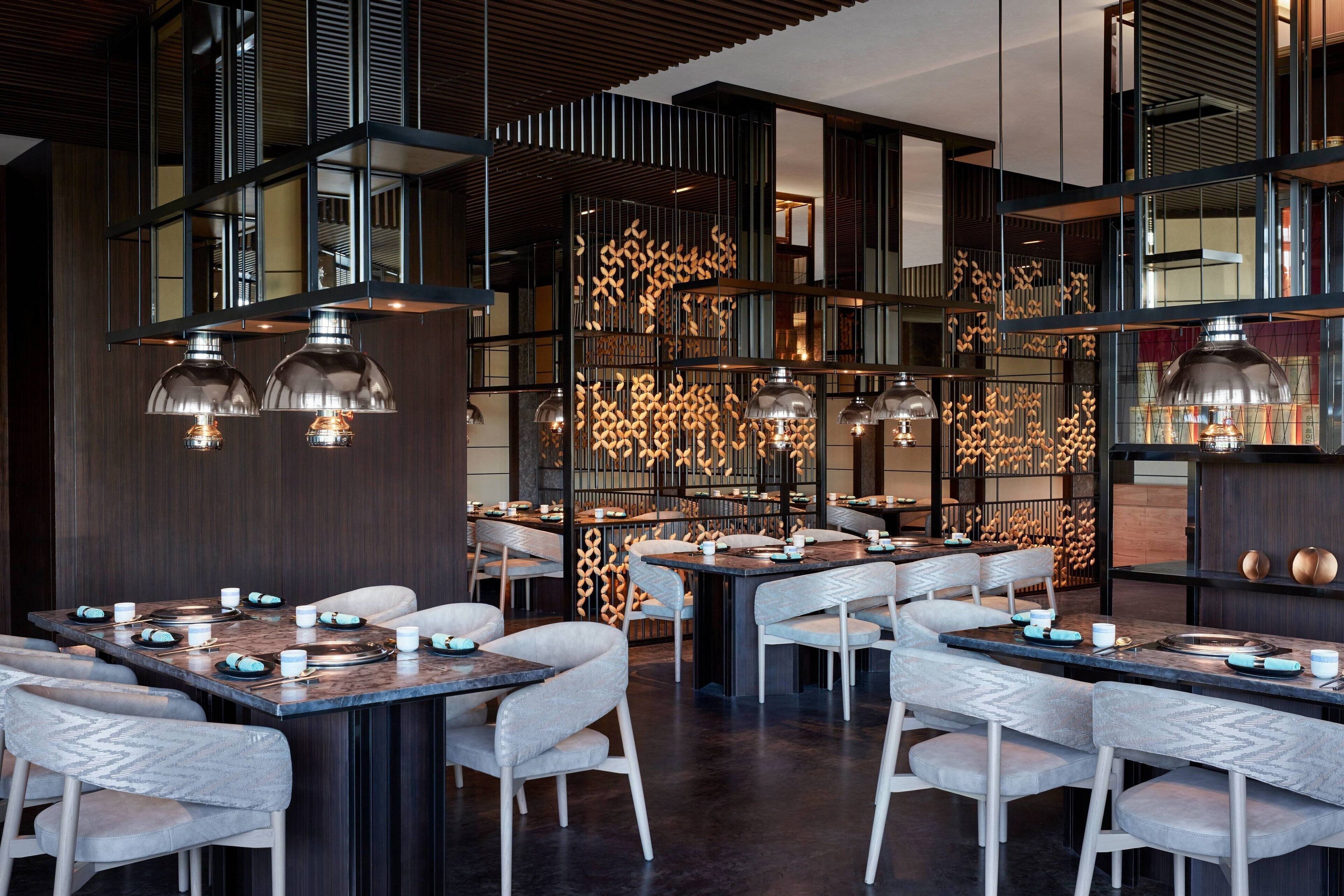 Un restaurant moderne avec un intérieur élégant, des lambris en bois foncé, de nombreuses tables et des luminaires contemporains.