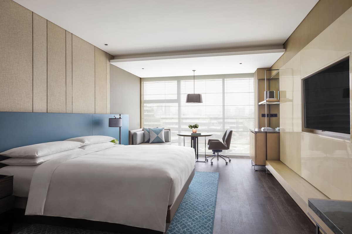 Moderni hotellihuone, jossa on suuri sänky, työpöytä, tuoli, pieni pöytä ja suuri ikkuna.