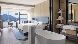 Habitación de hotel moderna con una cama grande, una bañera, un escritorio y vistas al mar.