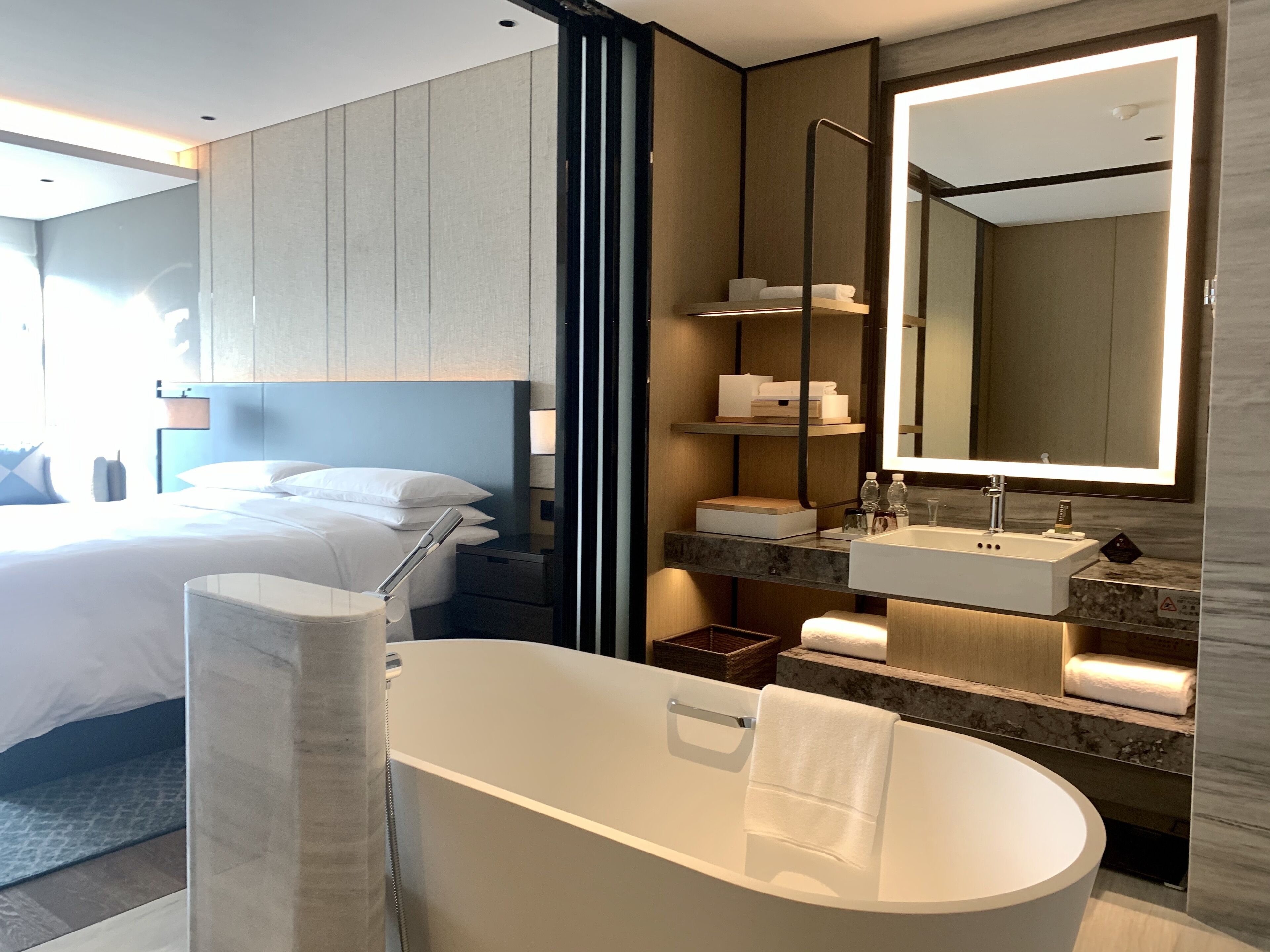 Une chambre d’hôtel moderne dotée d’un grand lit, d’une baignoire, d’une coiffeuse avec miroir et d’un espace douche.