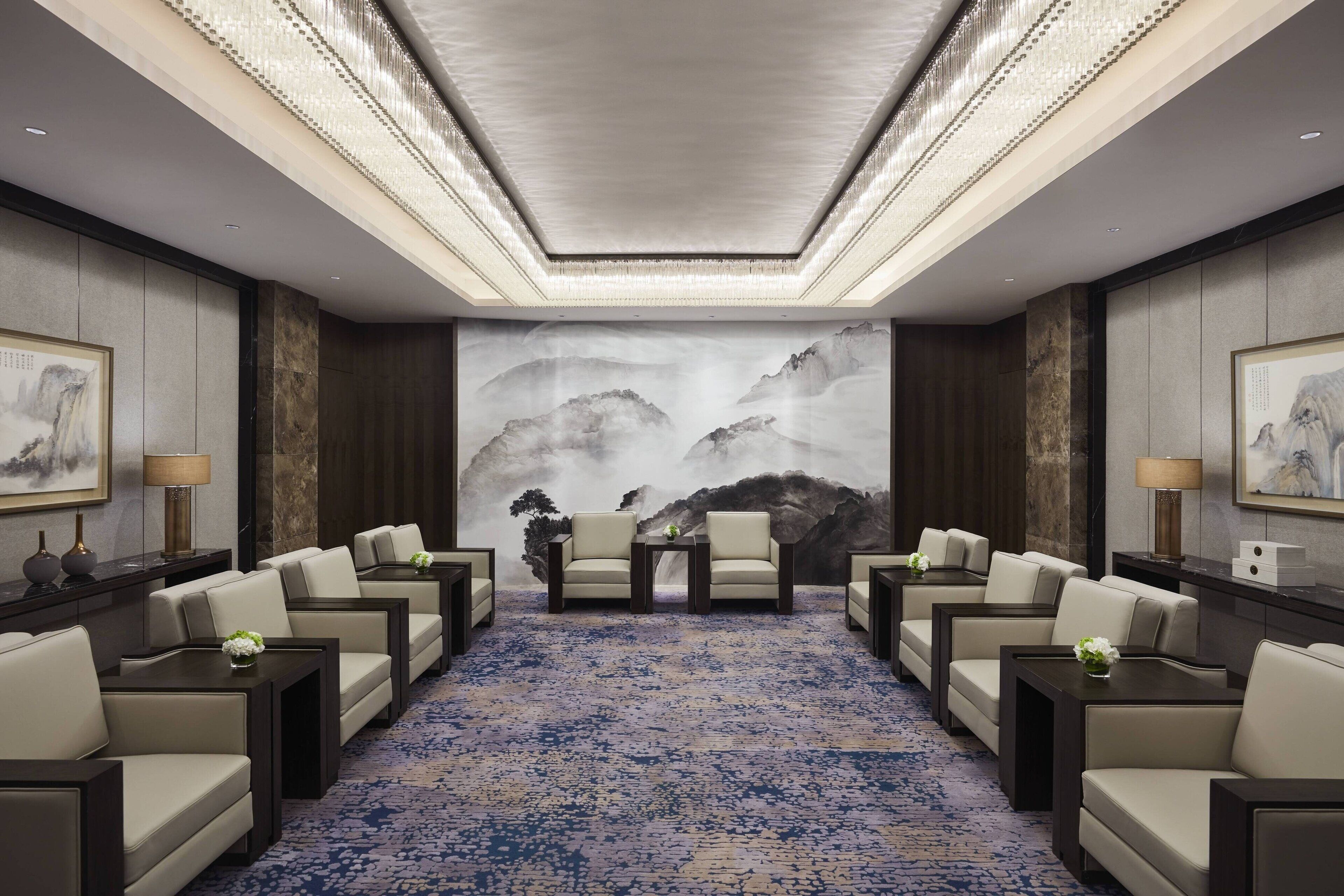 Un salón de conferencias con un gran mural de montañas, diversas disposiciones de asientos y una alfombra estampada.