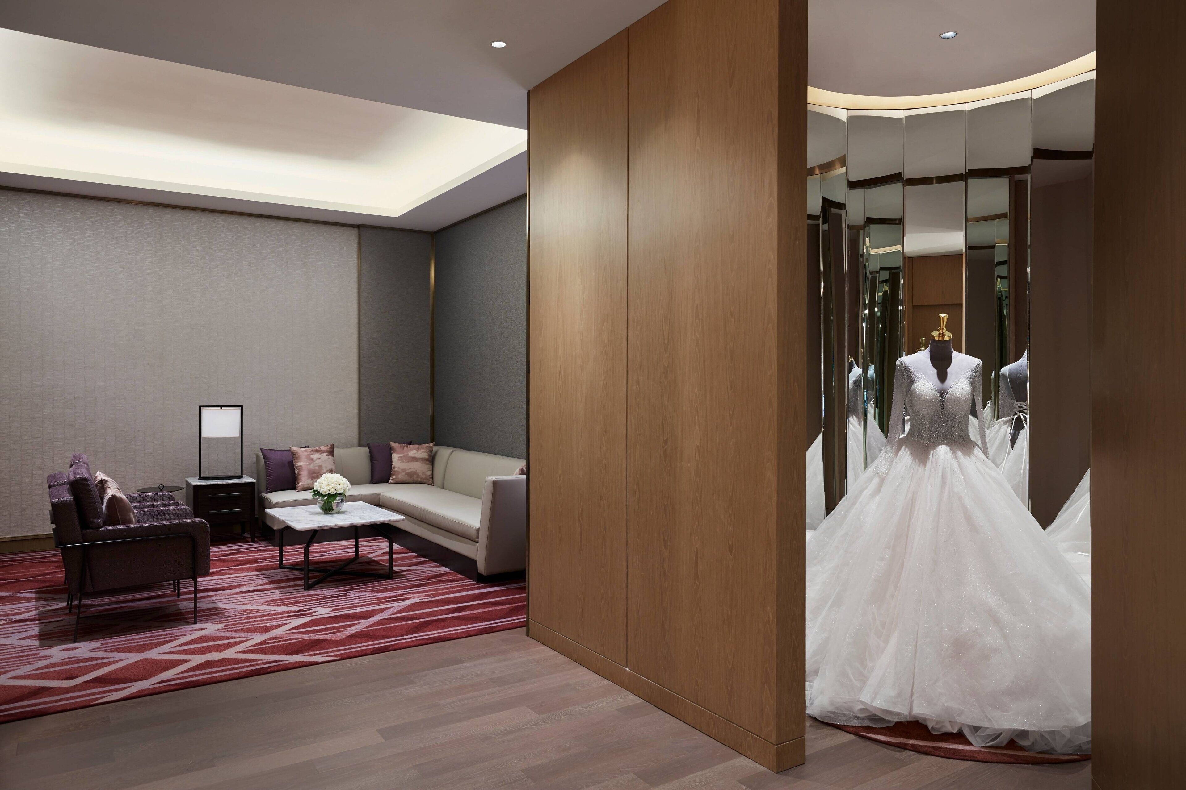 A modern hotel room with a sofa, a small table, and a dress on display in the mirror.