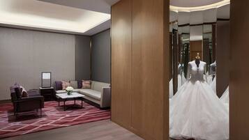 A modern hotel room with a sofa, a small table, and a dress on display in the mirror.