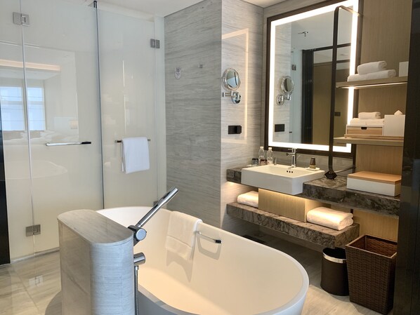 Un baño moderno con una bañera independiente, un espejo grande y un tocador con lavabo y toallero.