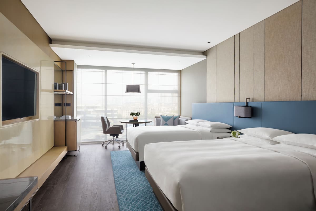 Hotellihuone, jossa on kaksi sänkyä, työpöytä, tuoli, televisio ja suuri ikkuna.
