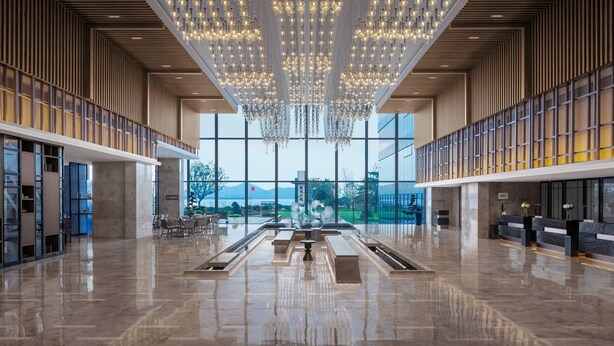 Un vestíbulo amplio con techos altos, candelabros modernos y vistas al exterior.