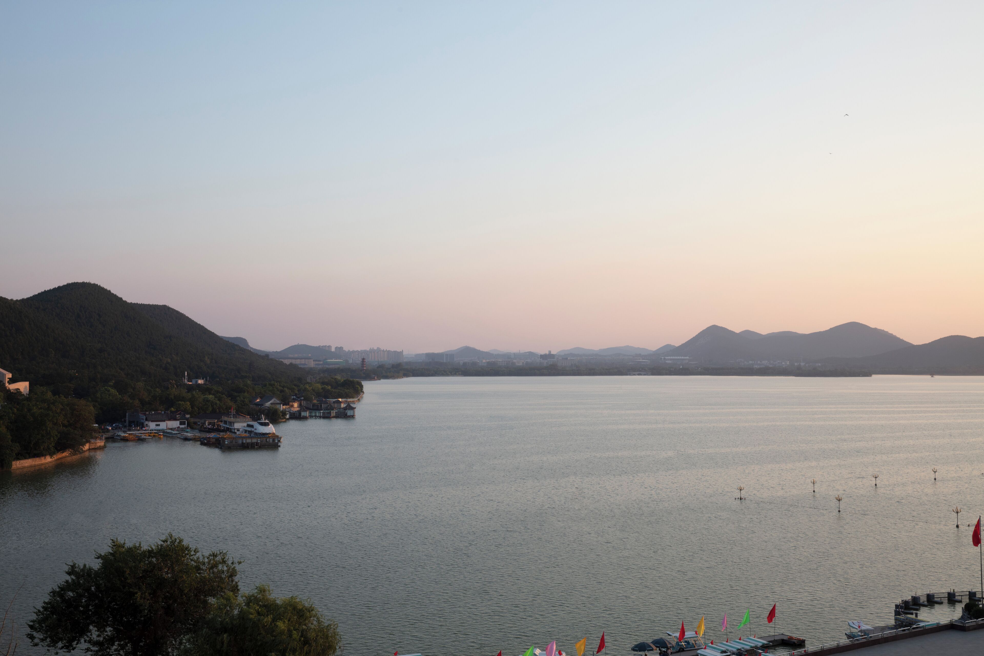 Un lago tranquilo con barcos, un embarcadero y colinas al fondo.