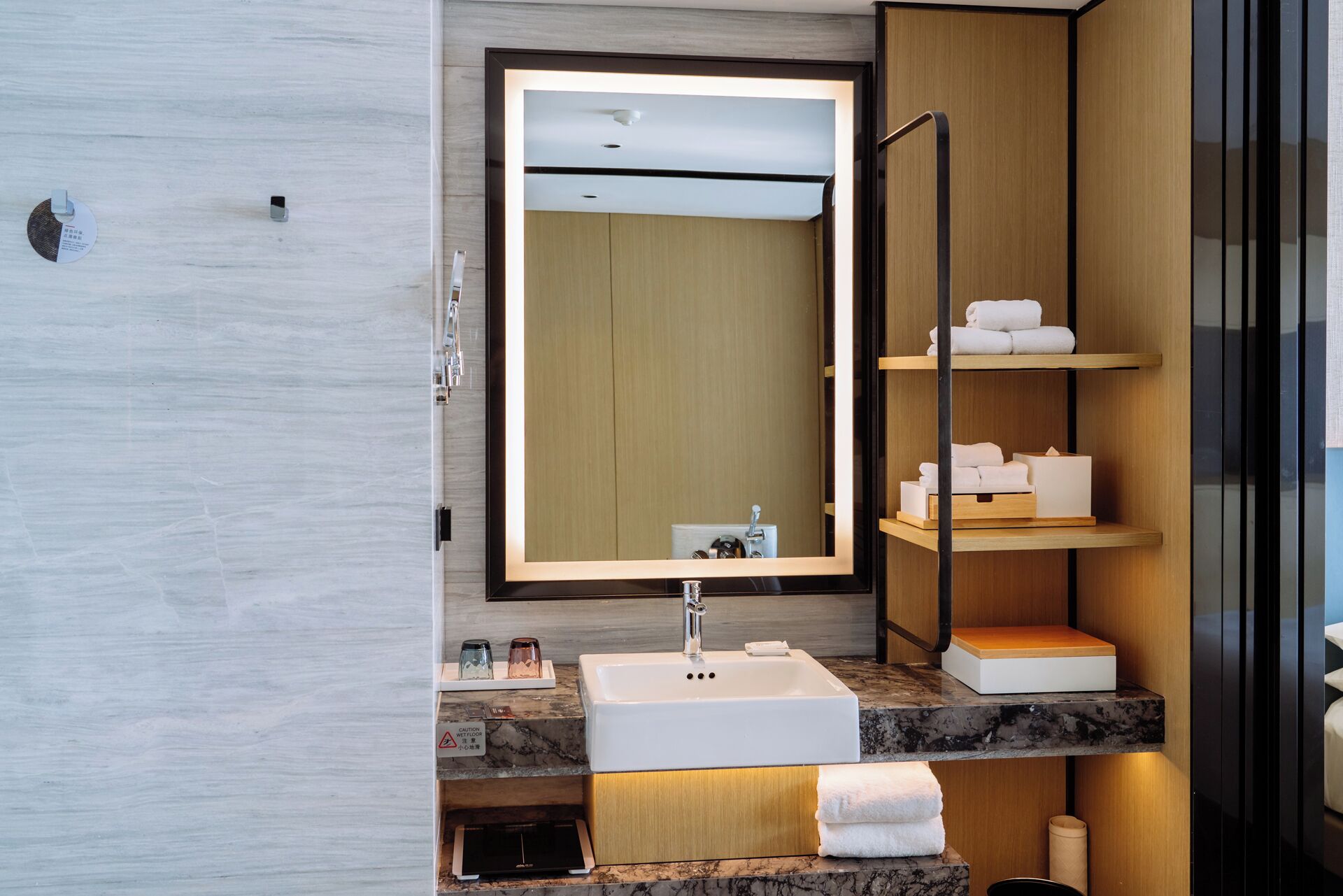 A modern bathroom with a marble sink, a large mirror, and shelves with toiletries.