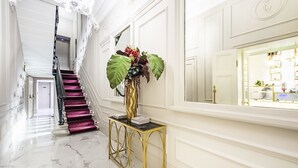 A grand hallway with a marble floor, a staircase with purple carpet, and a gold console table with a vase of flowers.