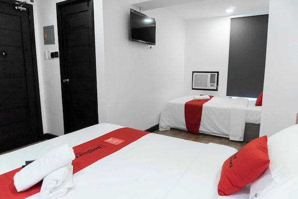 Ein Hotelzimmer mit zwei Betten, einem Fernseher, einer Klimaanlage und einem roten Handtuch auf dem Bett.
