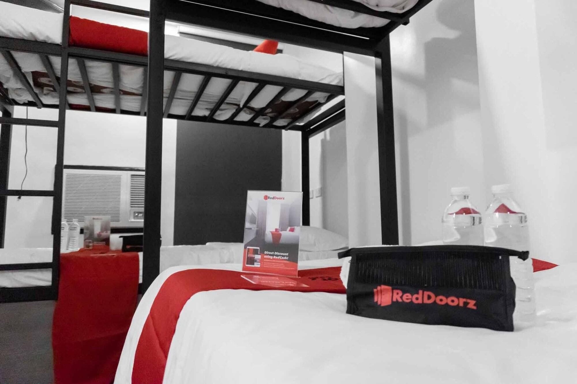 A hotel room with a bunk bed, a RedDoorz branded bag, and water bottles on the bedside table.