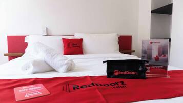 Ein Hotelzimmer mit einem ordentlich bezogenen Bett, einem roten und weißen Kissenpaar, einer Tasche von RedDoorz und einem Werbeständer von RedDoorz.
