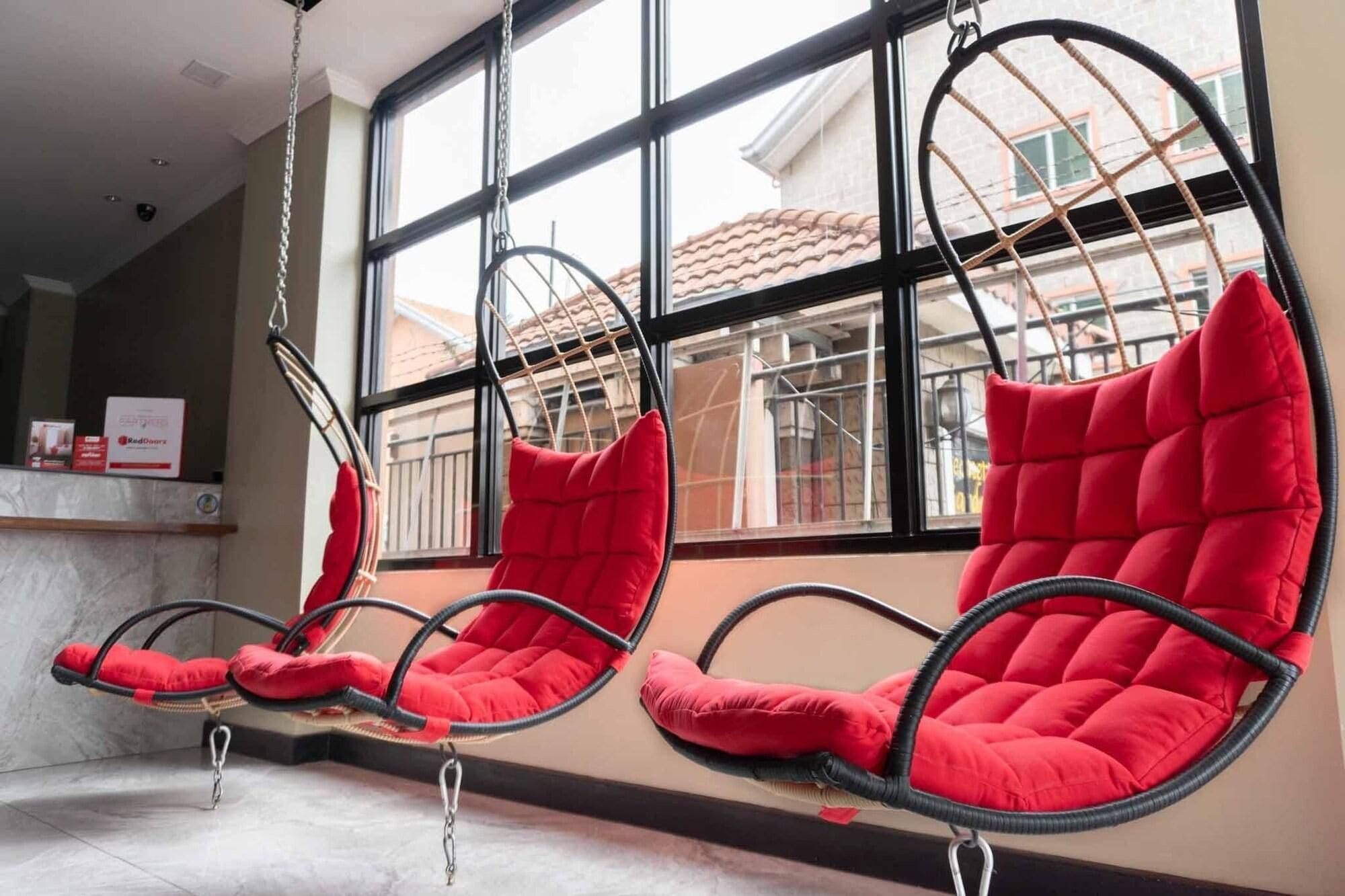 A row of red cushioned chairs suspended from the ceiling in a room with large windows.