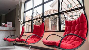 A row of red cushioned chairs suspended from the ceiling in a room with large windows.