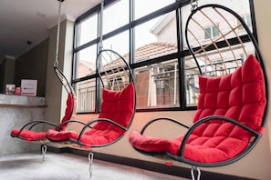 A row of red cushioned chairs suspended from the ceiling in a room with large windows. - Reddoorz Plus Near Bamboo Organ Las Pinas (Las Pinas)