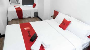 Een hotelkamer met twee bedden, elk voorzien van witte beddengoed en rode accenten. Op elk bed ligt een rood-wit dekbed en een rood kussen met tekst.