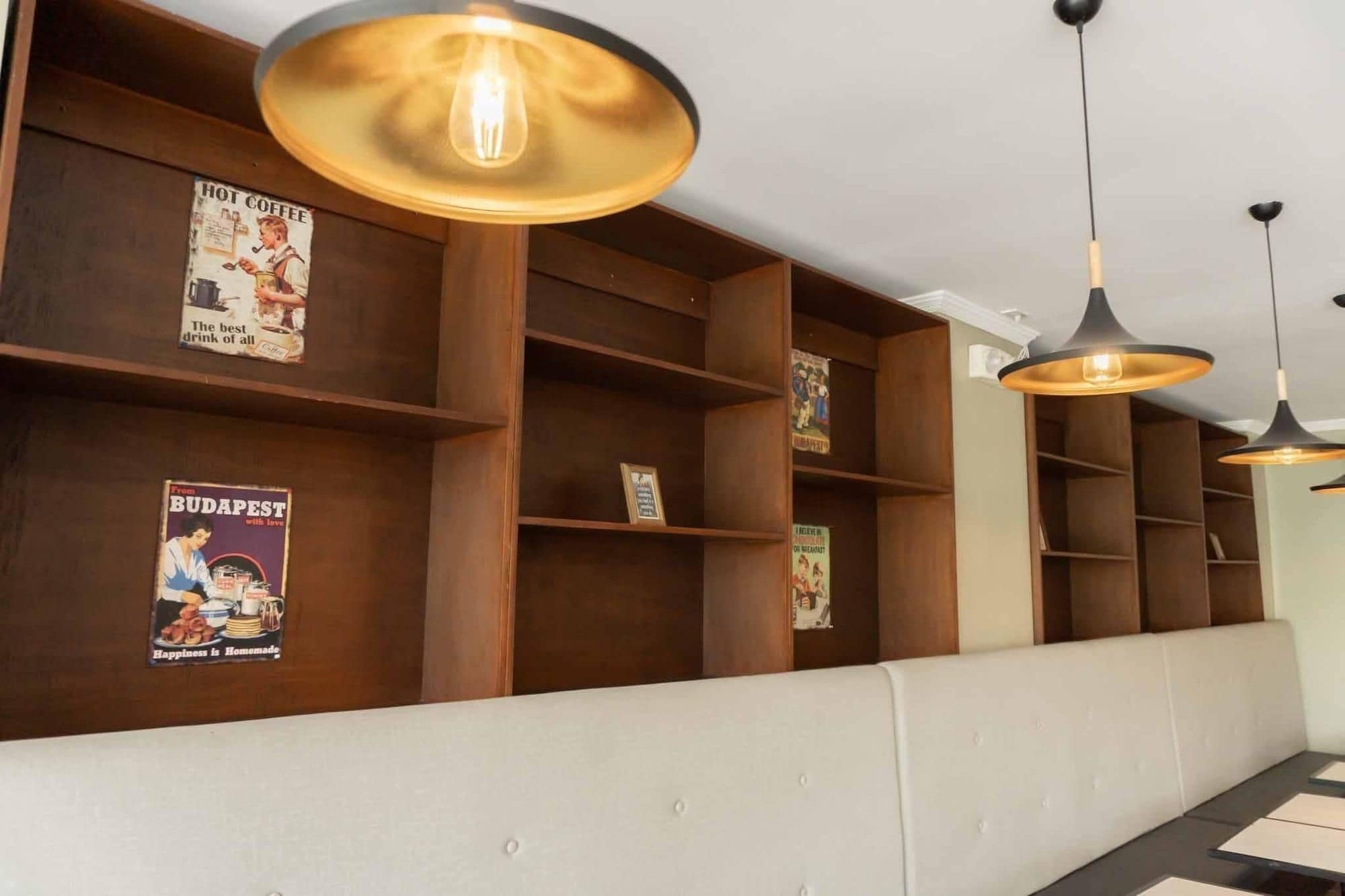 A hotel reception area with wooden shelving, a white bench, and pendant lighting.