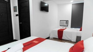 Een hotelkamer met twee bedden, een televisie, een airconditioningsysteem en een rode handdoek op het bed.