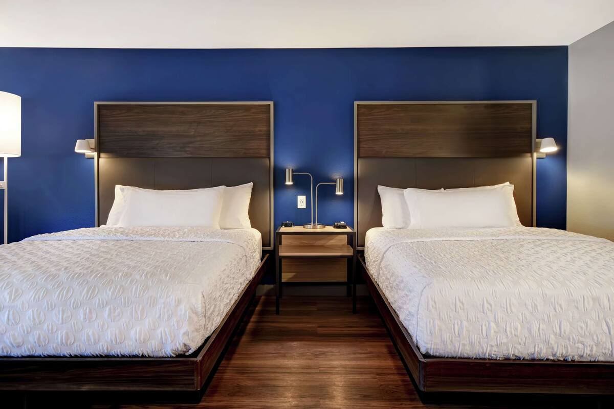 Habitación de hotel con dos camas, cabeceros de madera, ropa de cama blanca y lámparas de noche.