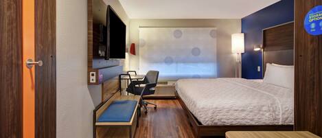 A hotel room with a bed, desk, chair, and a TV.