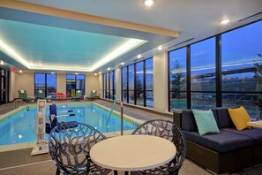 Una piscina interior con vistas al exterior, un área de estar con una mesa y un sofá con cojines.