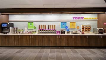A breakfast counter with various food items and a digital menu display.