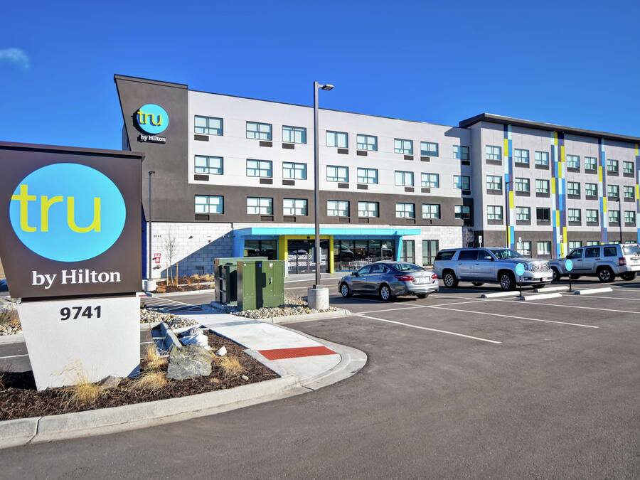 A hotel entrance with a sign reading "TRU by Hilton 9741" and a parking lot with several cars.