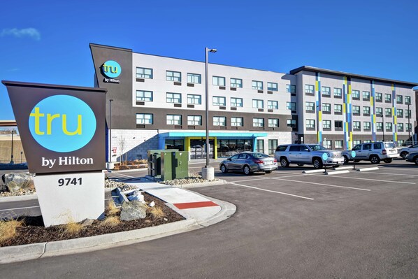 Entrada de un hotel con un letrero que dice 'TRU by Hilton 9741' y un estacionamiento con varios coches.