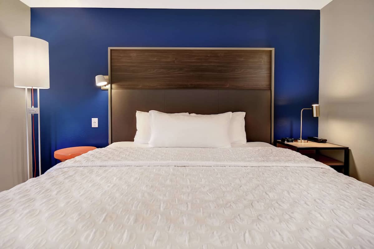 Una cama bien hecha con ropa de cama blanca, cabecera de madera y una mesita de noche con lámpara.