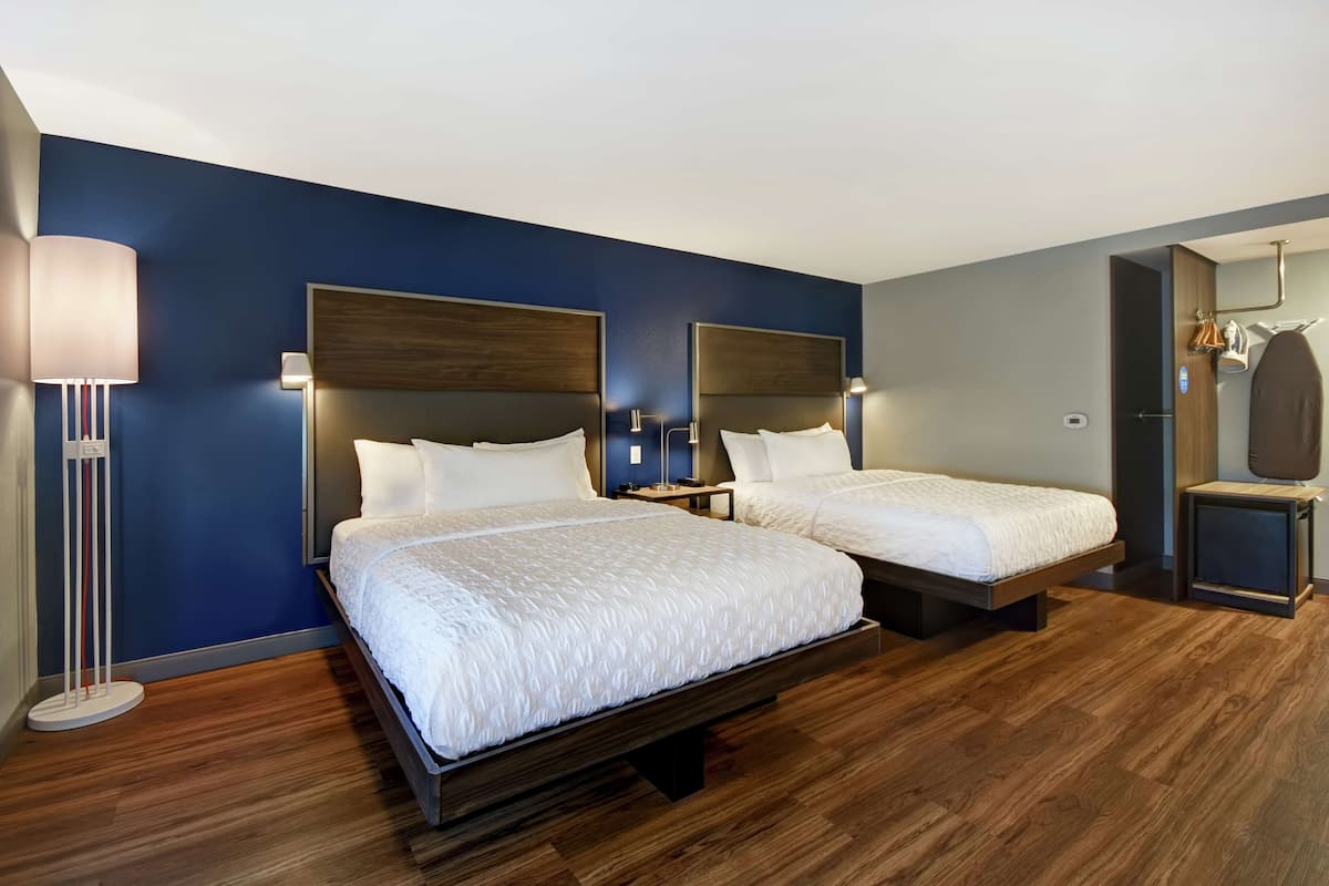 Habitación de hotel con dos camas, una mesita de noche, una lámpara y un armario.