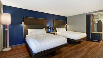 A hotel room with two beds, a bedside table, a lamp, and a wardrobe.