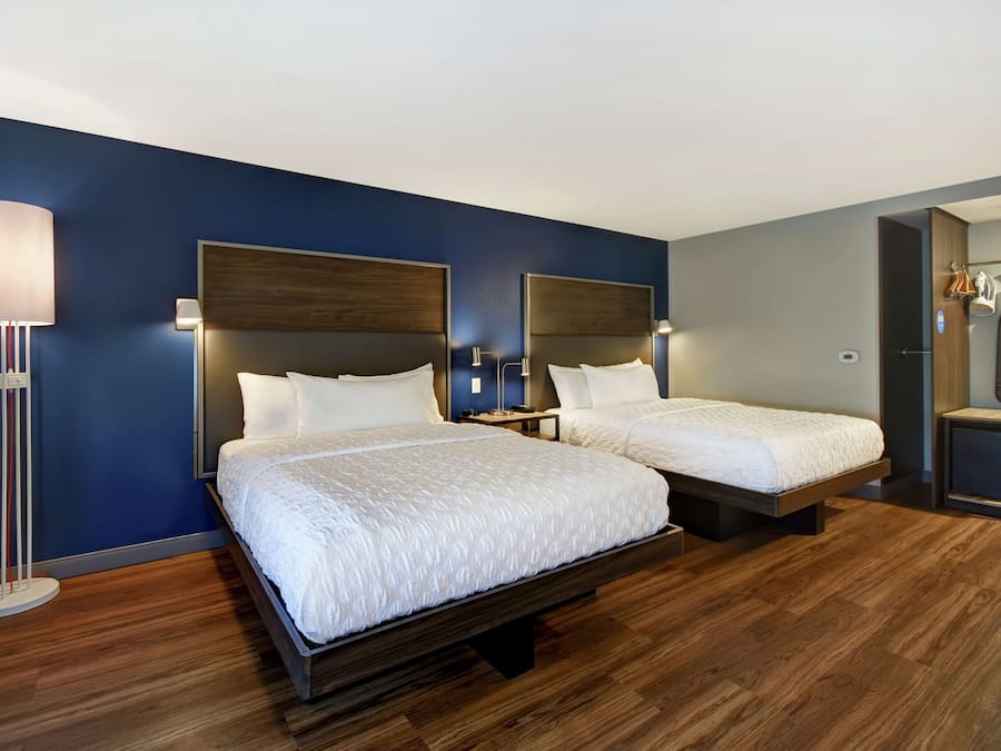A hotel room with two beds, a bedside table, a lamp, and a wardrobe.
