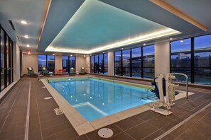 Una piscina interior con agua cristalina y azul, rodeada de amplios ventanales que ofrecen vistas al exterior.