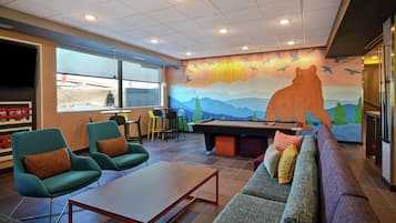 A lounge area with a pool table, green chairs, a sofa, and a mural depicting a bear and mountains.